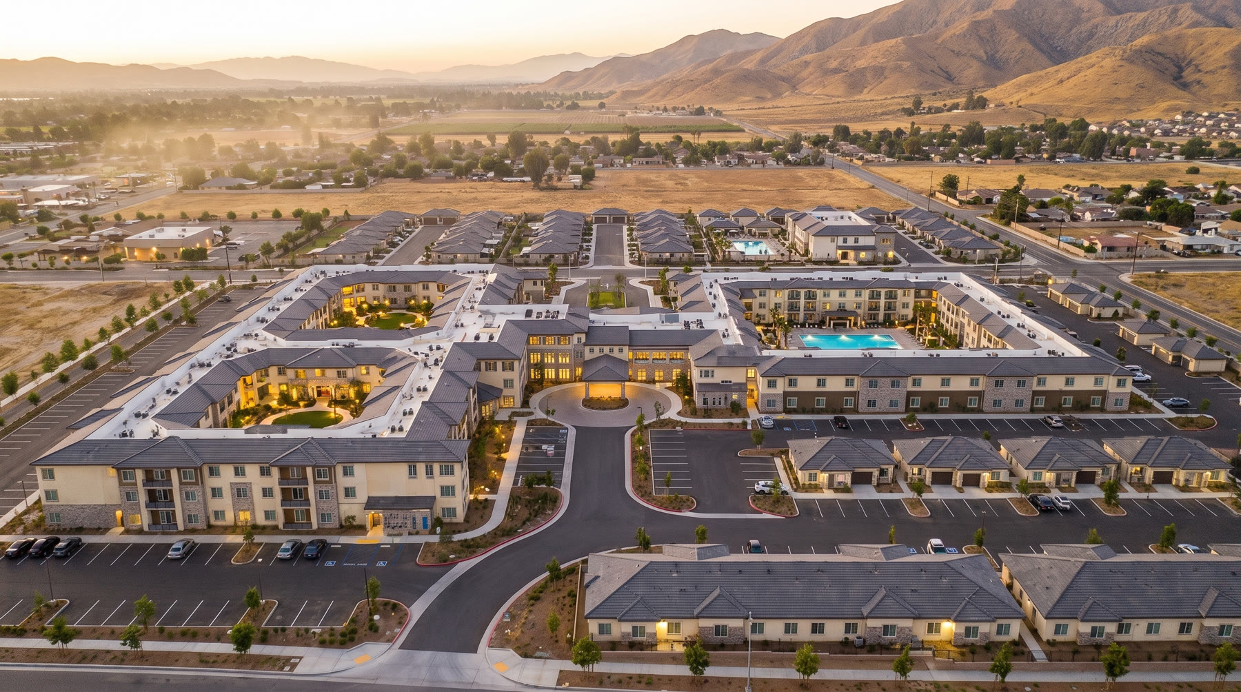 Aerial rendering of the MarchLife South senior living village at dusk, courtyard buildings glowing against the mountains